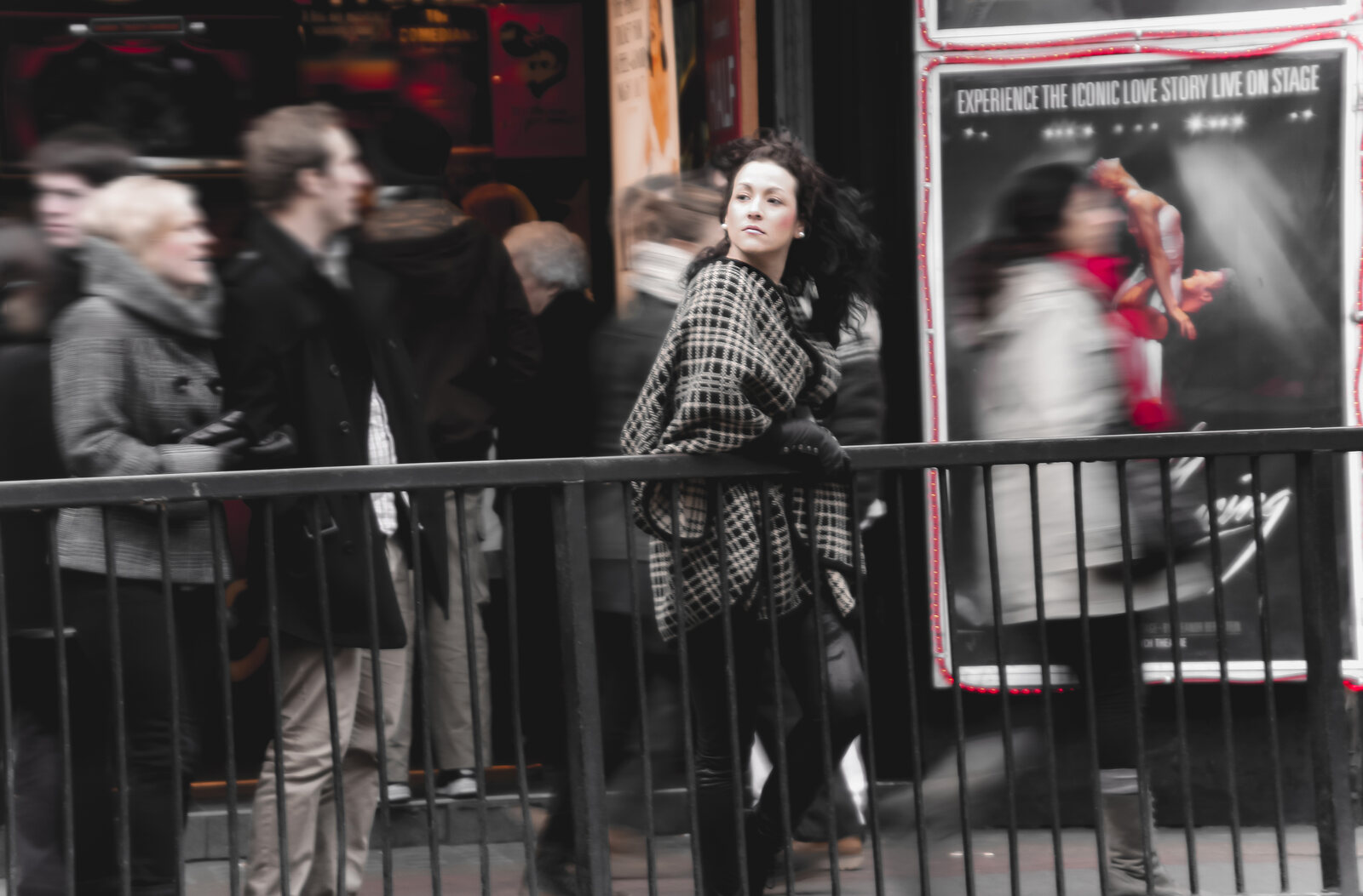 Model in a checked coat at a railing amid blurred theatre crowds